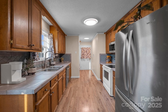 kitchen with sink, light hardwood / wood-style flooring, stainless steel appliances, tasteful backsplash, and tile counters