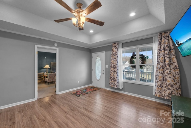 entryway with ceiling fan, a tray ceiling, wood-type flooring, and a textured ceiling