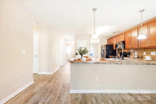 kitchen with light wood finished floors, tasteful backsplash, stainless steel microwave, light stone counters, and fridge with ice dispenser