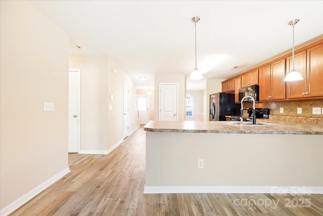 kitchen featuring tasteful backsplash, light wood-style floors, freestanding refrigerator, a sink, and a peninsula