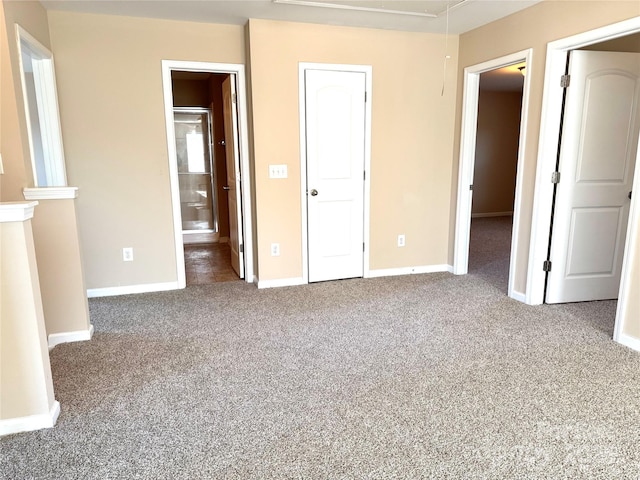 unfurnished bedroom featuring ensuite bath, carpet, attic access, and baseboards