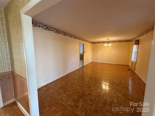 unfurnished room featuring a chandelier, dark parquet floors, and wood walls