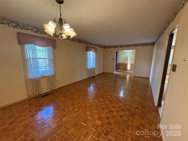 spare room featuring parquet flooring and a notable chandelier