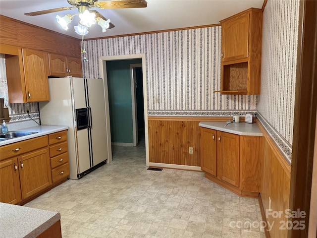 kitchen featuring sink, crown molding, wooden walls, ceiling fan, and white refrigerator with ice dispenser