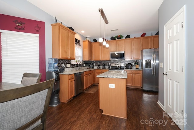 kitchen featuring stainless steel appliances, dark hardwood / wood-style floors, a center island, light stone countertops, and decorative light fixtures