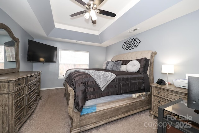 carpeted bedroom with ceiling fan and a tray ceiling