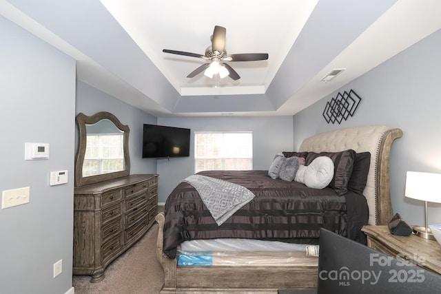 carpeted bedroom featuring ceiling fan and a tray ceiling