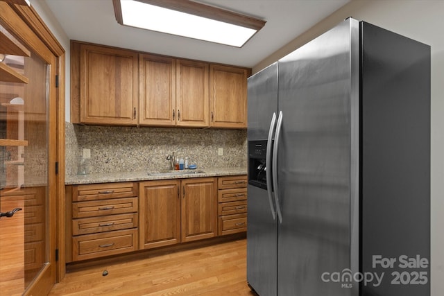 kitchen with sink, backsplash, light stone counters, stainless steel fridge with ice dispenser, and light hardwood / wood-style flooring