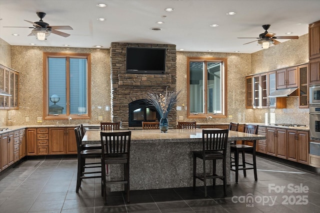 kitchen featuring decorative backsplash, appliances with stainless steel finishes, a stone fireplace, and a breakfast bar area