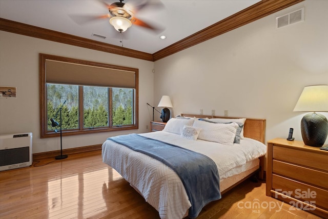 bedroom featuring ceiling fan, ornamental molding, heating unit, and light hardwood / wood-style flooring