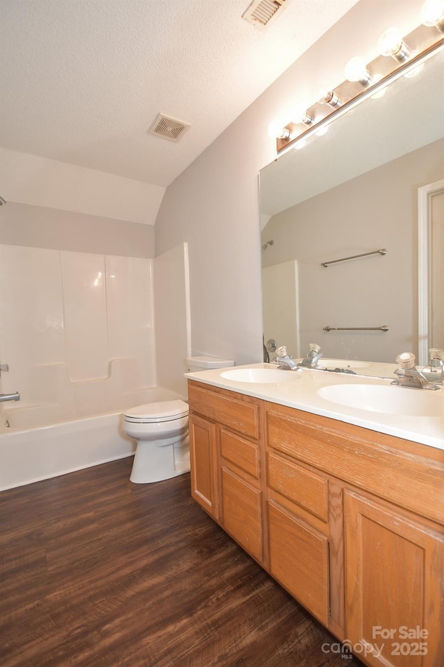 full bathroom featuring  shower combination, vanity, wood-type flooring, a textured ceiling, and toilet