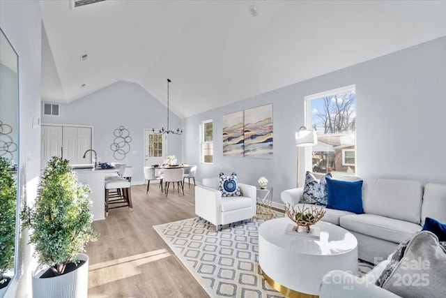 living room with a notable chandelier, lofted ceiling, light hardwood / wood-style floors, and plenty of natural light