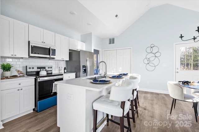 kitchen featuring sink, a kitchen island with sink, white cabinetry, stainless steel appliances, and a kitchen bar