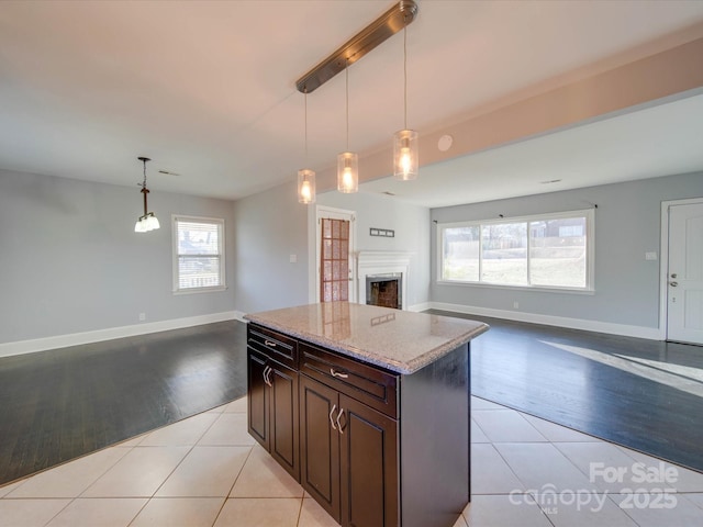 kitchen featuring dark brown cabinets, light tile patterned floors, light stone counters, and decorative light fixtures