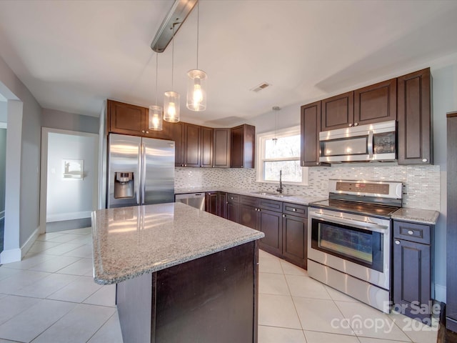 kitchen featuring pendant lighting, sink, appliances with stainless steel finishes, light stone countertops, and a kitchen island