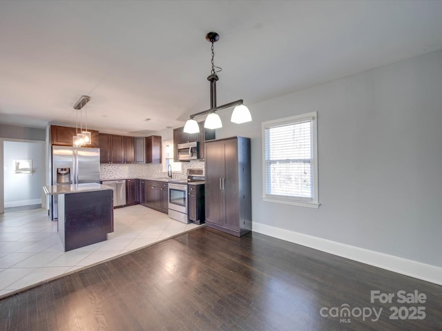 kitchen with tasteful backsplash, appliances with stainless steel finishes, a center island, and hanging light fixtures