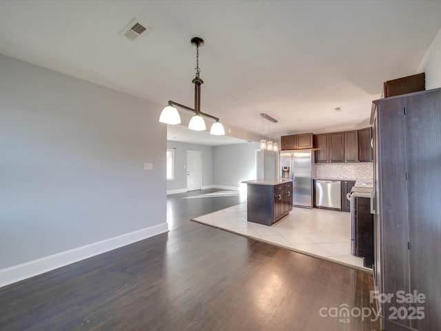 kitchen with light hardwood / wood-style flooring, stainless steel appliances, tasteful backsplash, a kitchen island, and decorative light fixtures