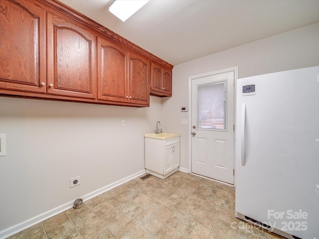 laundry room featuring electric dryer hookup, sink, cabinets, and a textured ceiling