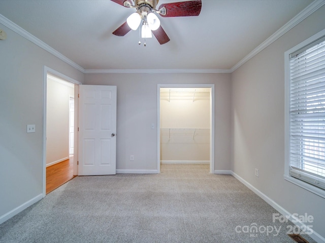 unfurnished bedroom featuring crown molding, a walk in closet, light carpet, a closet, and ceiling fan