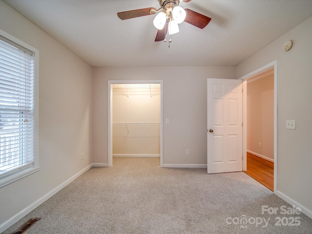 unfurnished bedroom with a spacious closet, light colored carpet, ceiling fan, and a closet