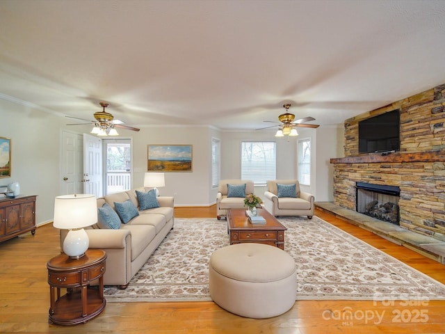 living room featuring crown molding, ceiling fan, a fireplace, and light hardwood / wood-style flooring