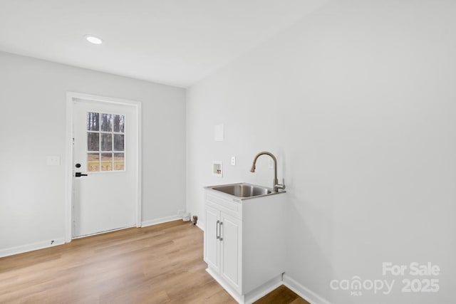 clothes washing area featuring hookup for a washing machine, sink, cabinets, and light hardwood / wood-style floors