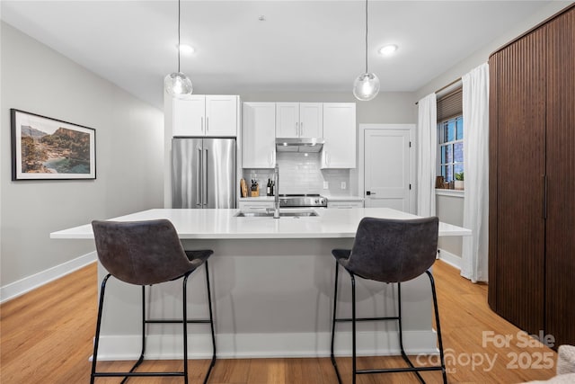 kitchen featuring pendant lighting, sink, white cabinetry, high quality fridge, and an island with sink