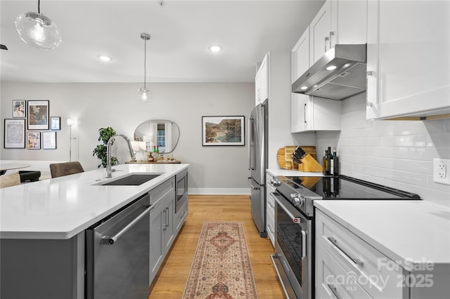 kitchen featuring appliances with stainless steel finishes, decorative light fixtures, sink, a kitchen island with sink, and wall chimney range hood