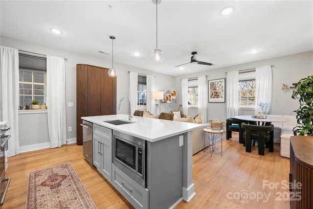 kitchen with gray cabinets, pendant lighting, an island with sink, sink, and stainless steel appliances