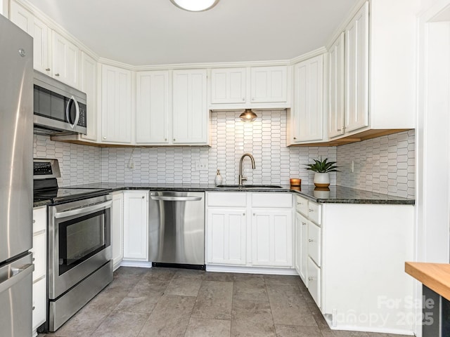 kitchen with white cabinetry, sink, backsplash, dark stone counters, and stainless steel appliances