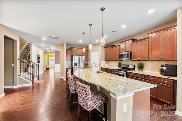 kitchen with a center island with sink, stainless steel appliances, visible vents, decorative backsplash, and a sink