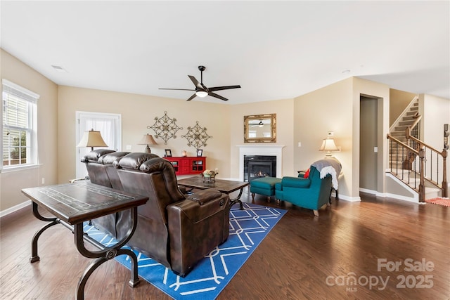 living room with stairway, a ceiling fan, a glass covered fireplace, wood finished floors, and baseboards