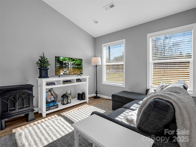 living room featuring vaulted ceiling, a wood stove, and hardwood / wood-style floors