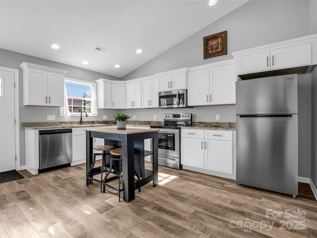 kitchen featuring stone counters, appliances with stainless steel finishes, high vaulted ceiling, white cabinetry, and sink