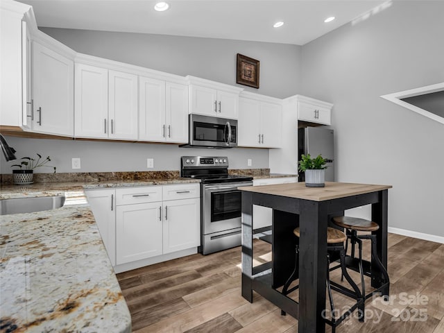 kitchen featuring sink, white cabinetry, high vaulted ceiling, appliances with stainless steel finishes, and light stone countertops