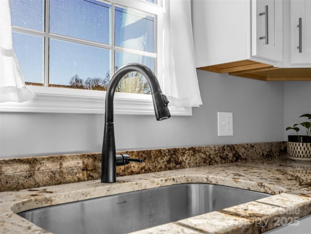 interior details with white cabinetry, sink, and light stone counters