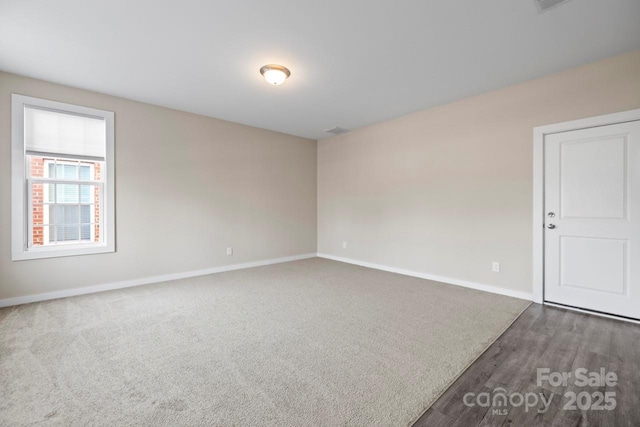 spare room with baseboards and dark colored carpet