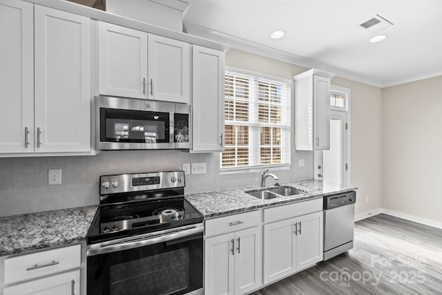 kitchen with stainless steel appliances, a sink, white cabinetry, light stone countertops, and tasteful backsplash