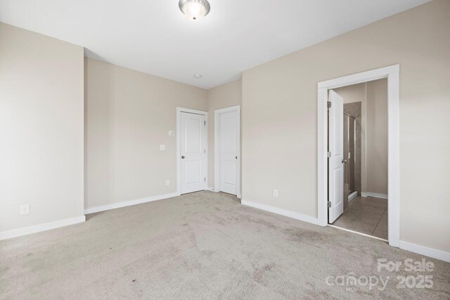 unfurnished bedroom with baseboards, ensuite bath, and light colored carpet