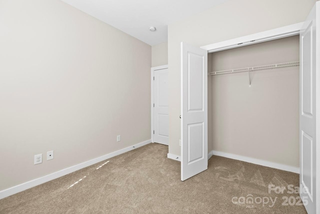 unfurnished bedroom with a closet, light colored carpet, and baseboards