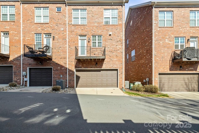 view of front of home featuring a garage, driveway, brick siding, and cooling unit