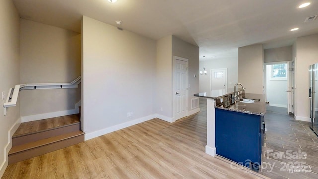 kitchen with sink, blue cabinetry, light hardwood / wood-style floors, and light stone countertops