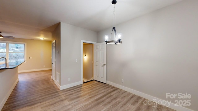 unfurnished dining area featuring ceiling fan with notable chandelier and light wood-type flooring