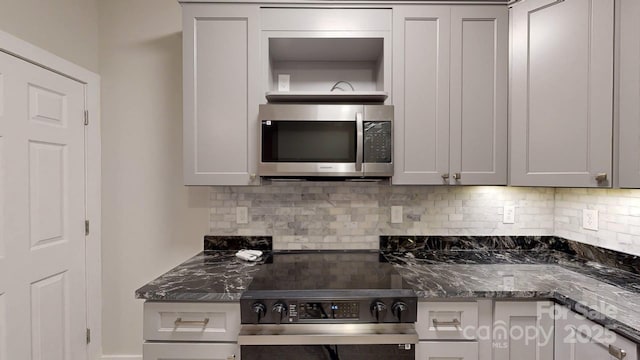 kitchen featuring tasteful backsplash, dark stone counters, stove, and gray cabinetry