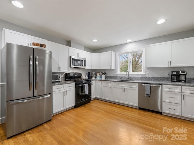 kitchen with stainless steel appliances, sink, white cabinets, and light hardwood / wood-style flooring