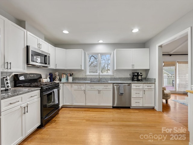 kitchen with appliances with stainless steel finishes, sink, white cabinets, and light hardwood / wood-style flooring