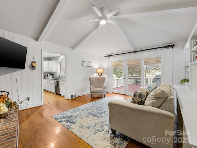 living room with sink, vaulted ceiling with beams, light hardwood / wood-style flooring, wooden walls, and ceiling fan