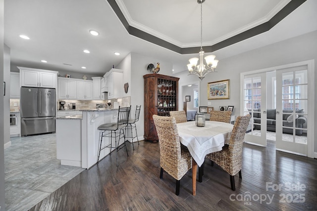 dining space featuring dark wood-type flooring, ornamental molding, a tray ceiling, and an inviting chandelier