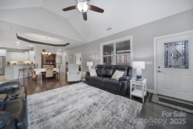 living room featuring dark wood-type flooring, vaulted ceiling, a raised ceiling, and ceiling fan with notable chandelier