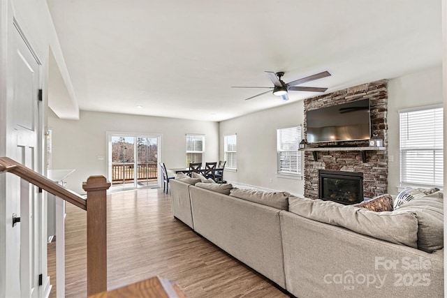 living room with a fireplace, ceiling fan, and light wood-type flooring